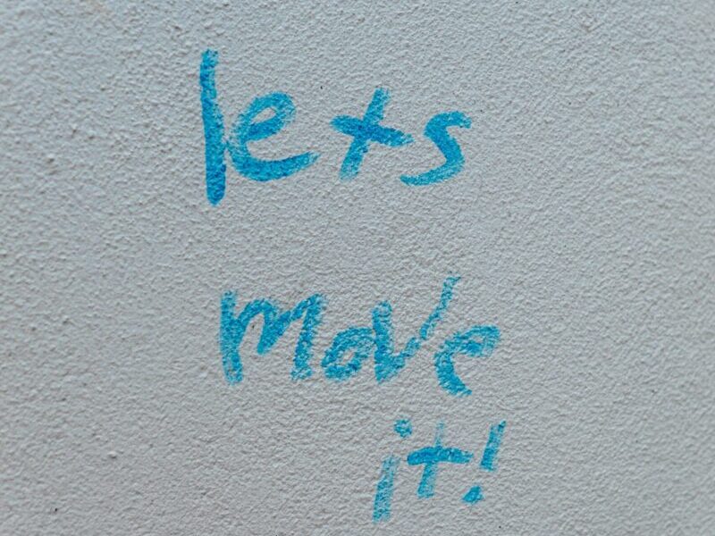 Close-up of blue text 'lets move it!' on a white wall, inspirational graffiti.